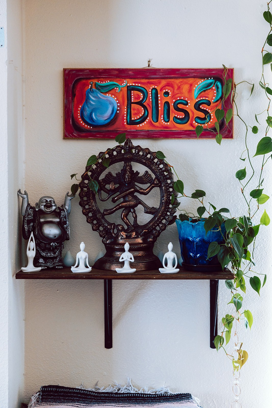 Bliss sign above a shelf of Buddha and dancing Shiva statues with trailing plant