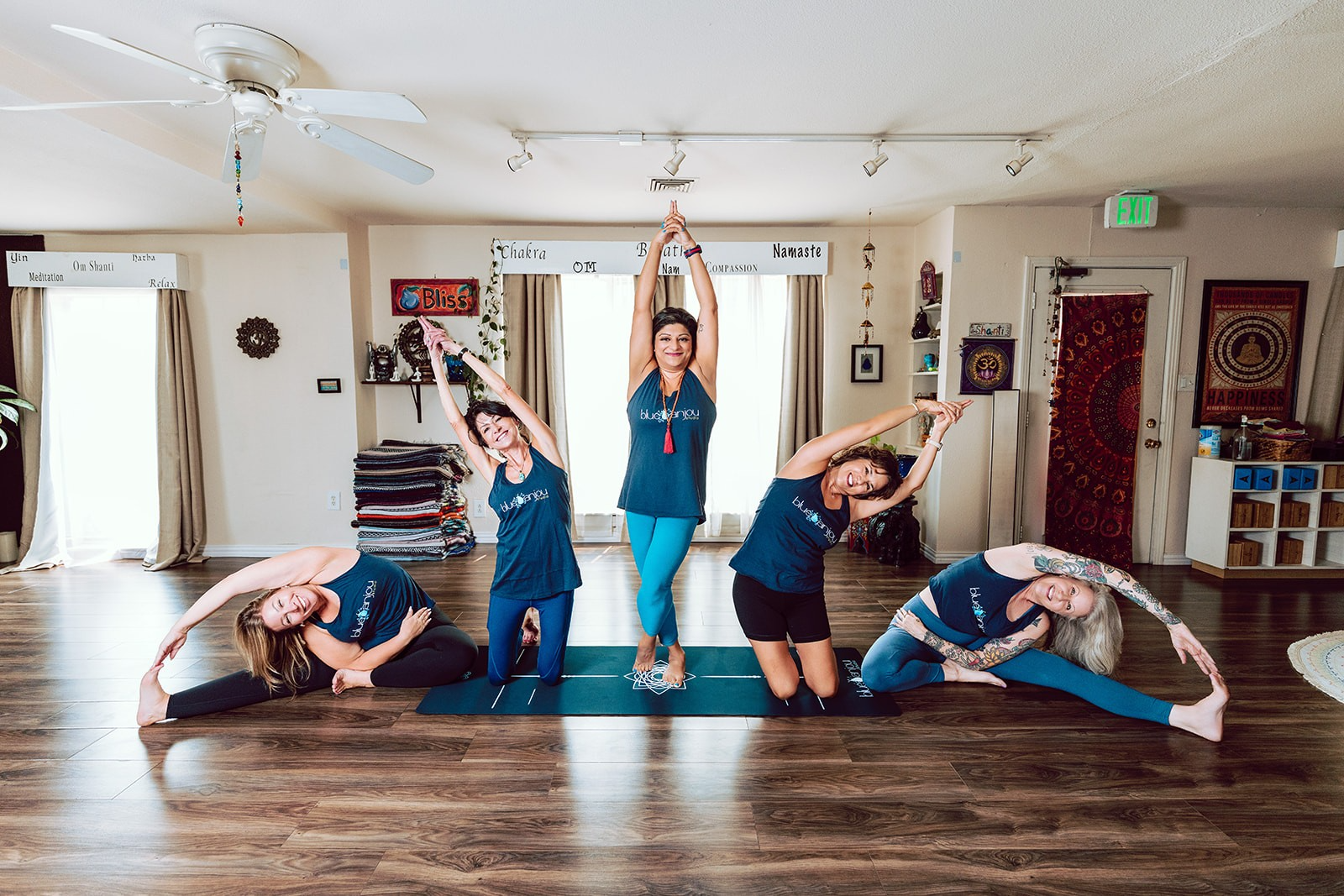 Five Blue Anjou teachers practicing side stretches together in the sunlit studio