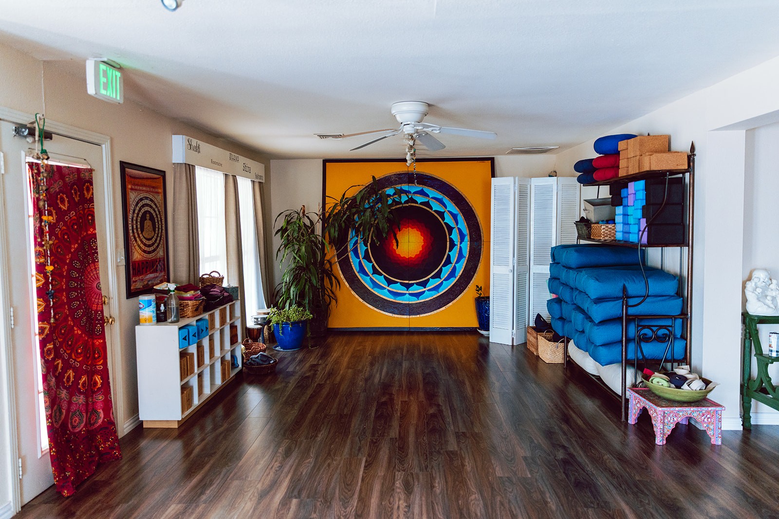 Open practice room with the orange mandala mural and shelves of bolsters