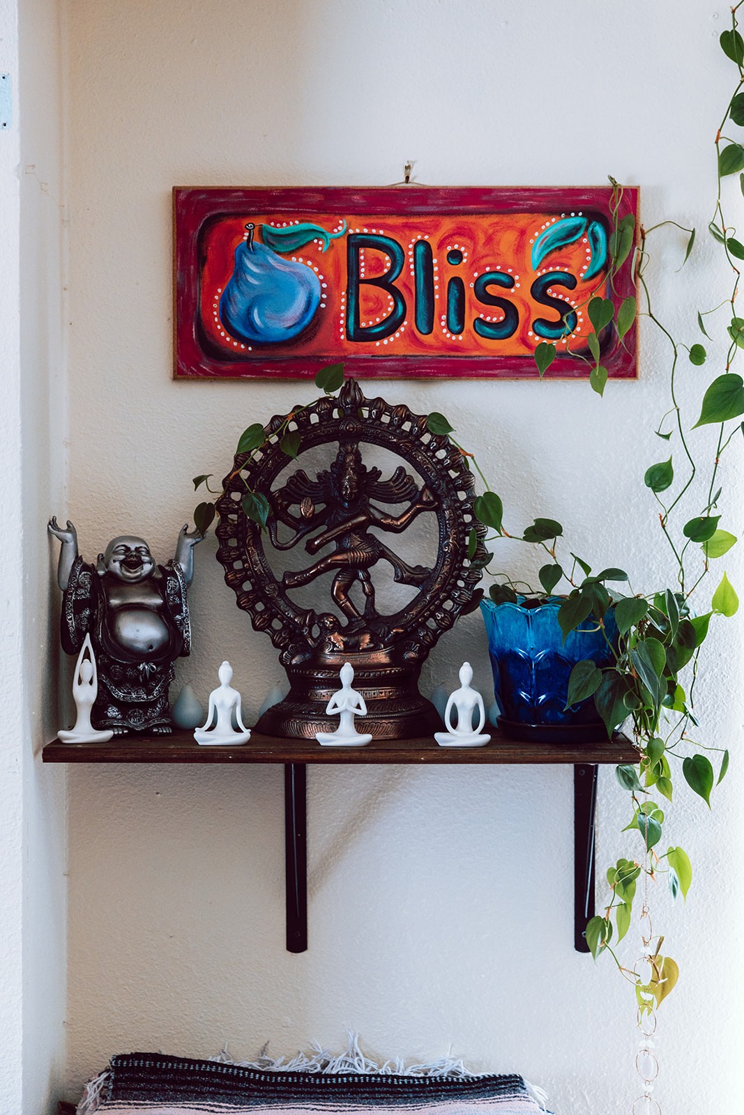 Shelf with laughing Buddha and dancing Shiva statues under a Bliss sign